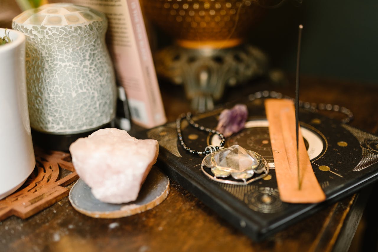 about-img Warm-toned composition featuring incense, rose quartz, and mystical elements on a wooden surface.