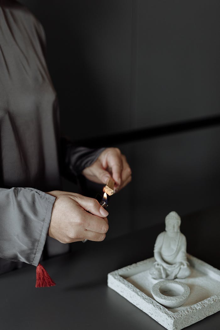 gallery-3 A person is lighting incense near a Buddha statue, suggesting a moment of meditation or ritual.