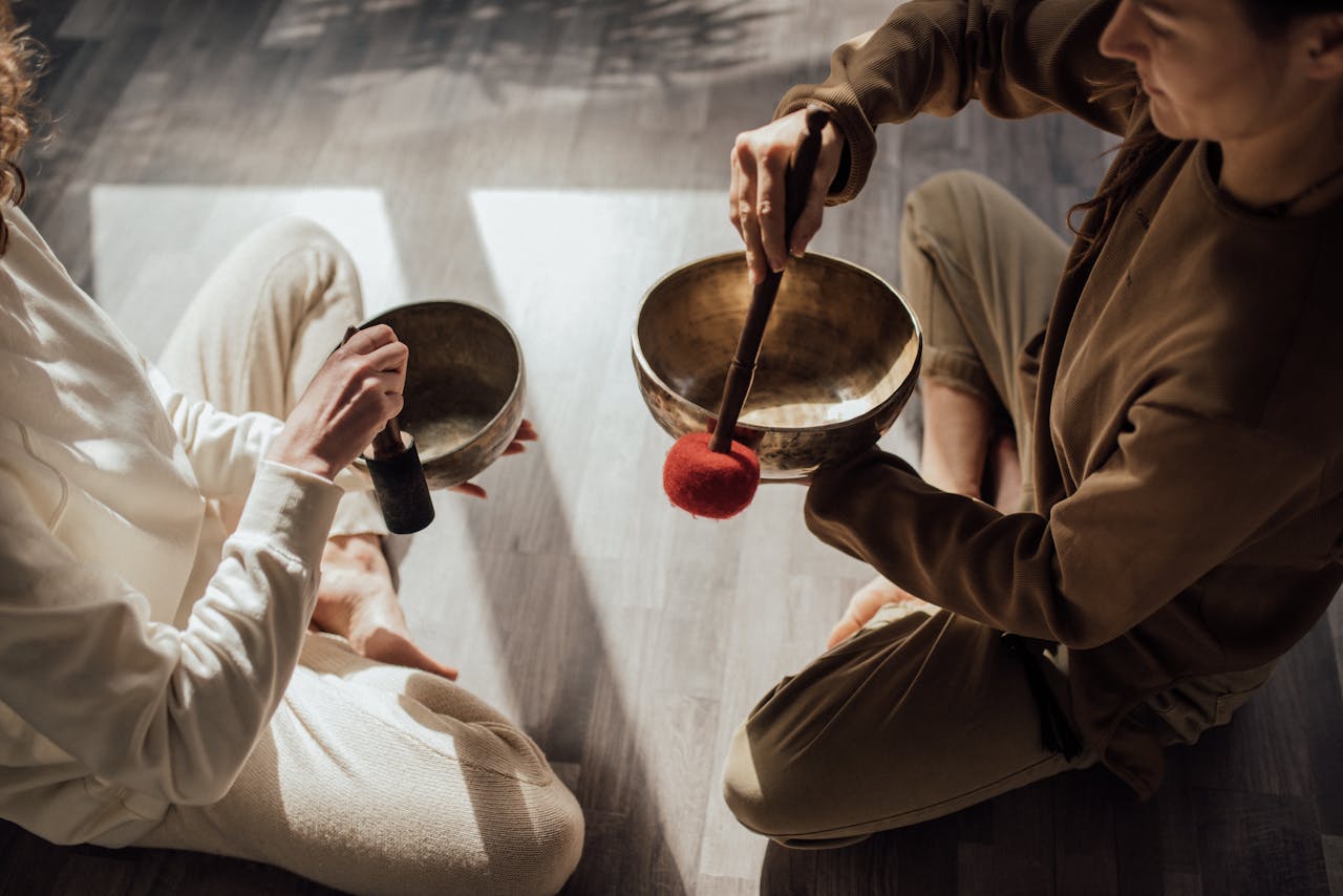 gallery-2 Two women meditating with Tibetan singing bowls in a peaceful indoor setting.