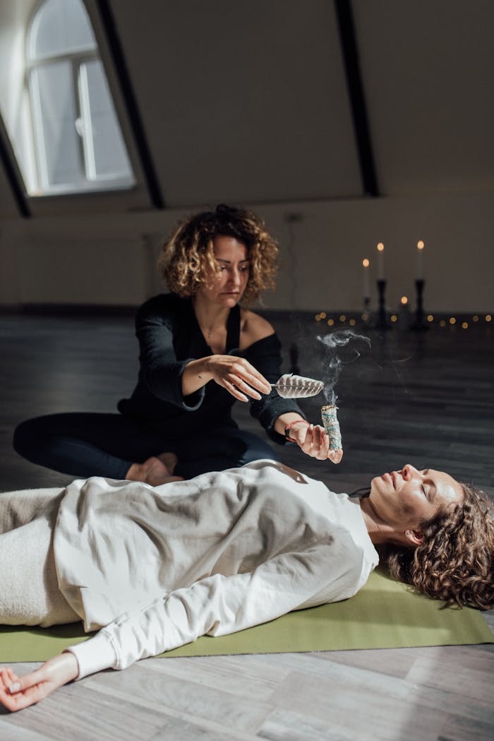 gallery-4 A woman performs a healing ritual with sage smoke indoors, aiding in meditation and tranquility.