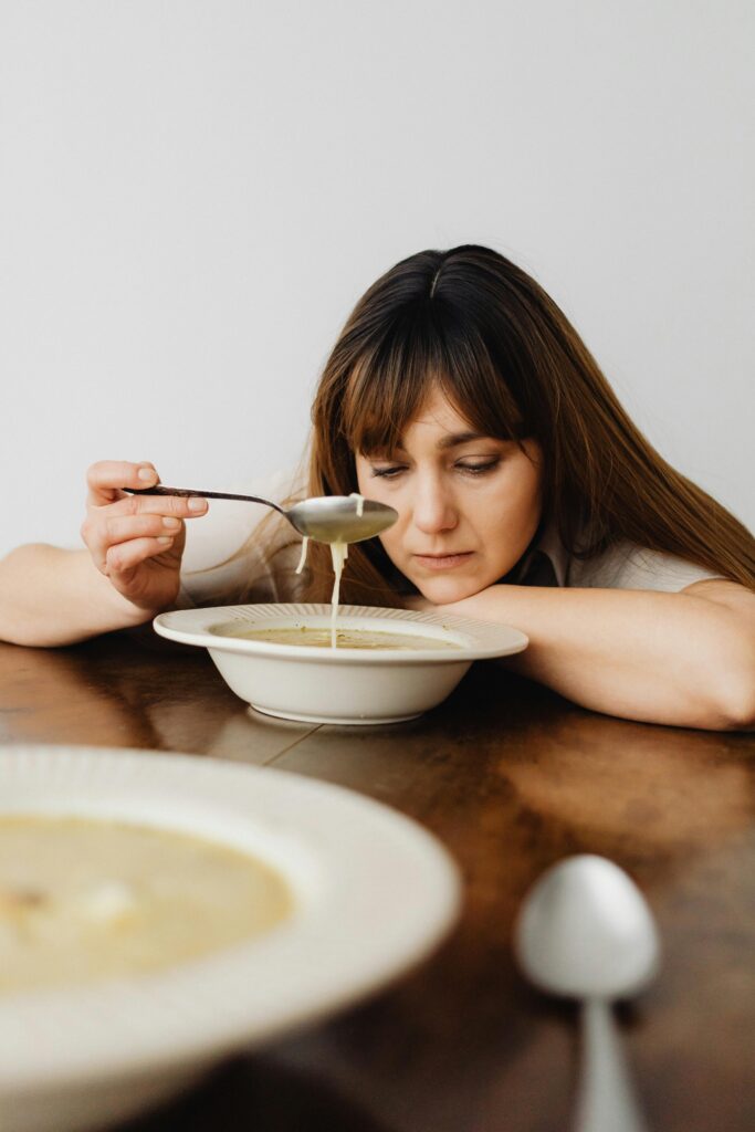 pexels photo 7272609 7272609 An adult woman deeply lost in thought while holding a spoonful of soup at a table.