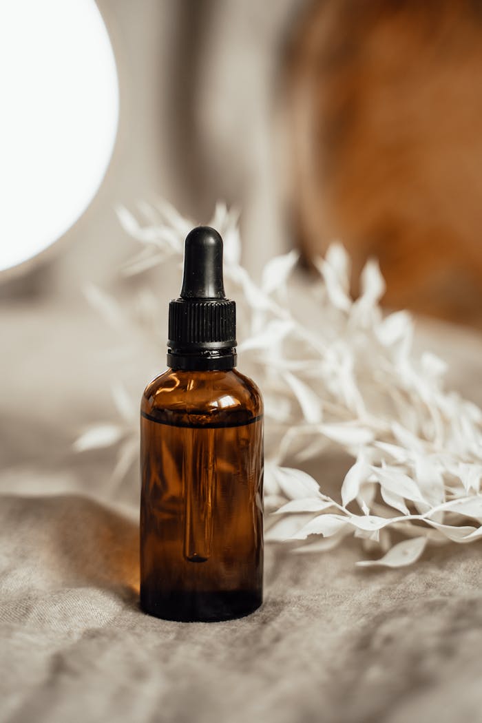 our-experience Elegant amber glass dropper bottle with organic oil and white botanicals on a cozy linen background.
