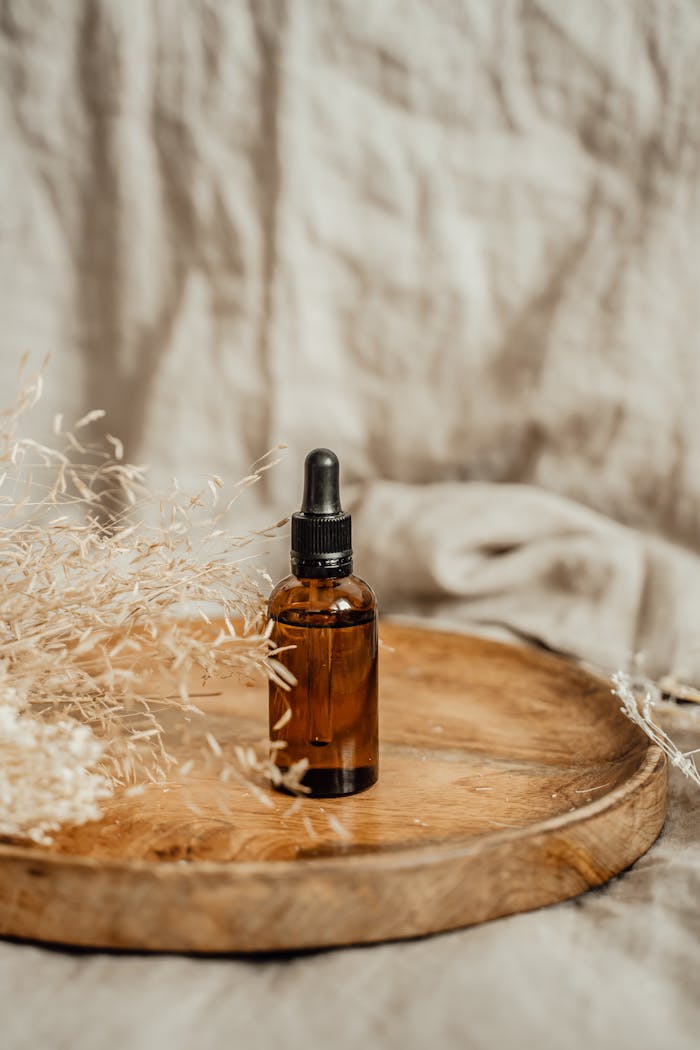 gallery-5 Brown glass cosmetic bottle with dropper on a wooden tray, surrounded by dried plants, perfect for spa and beauty themes.