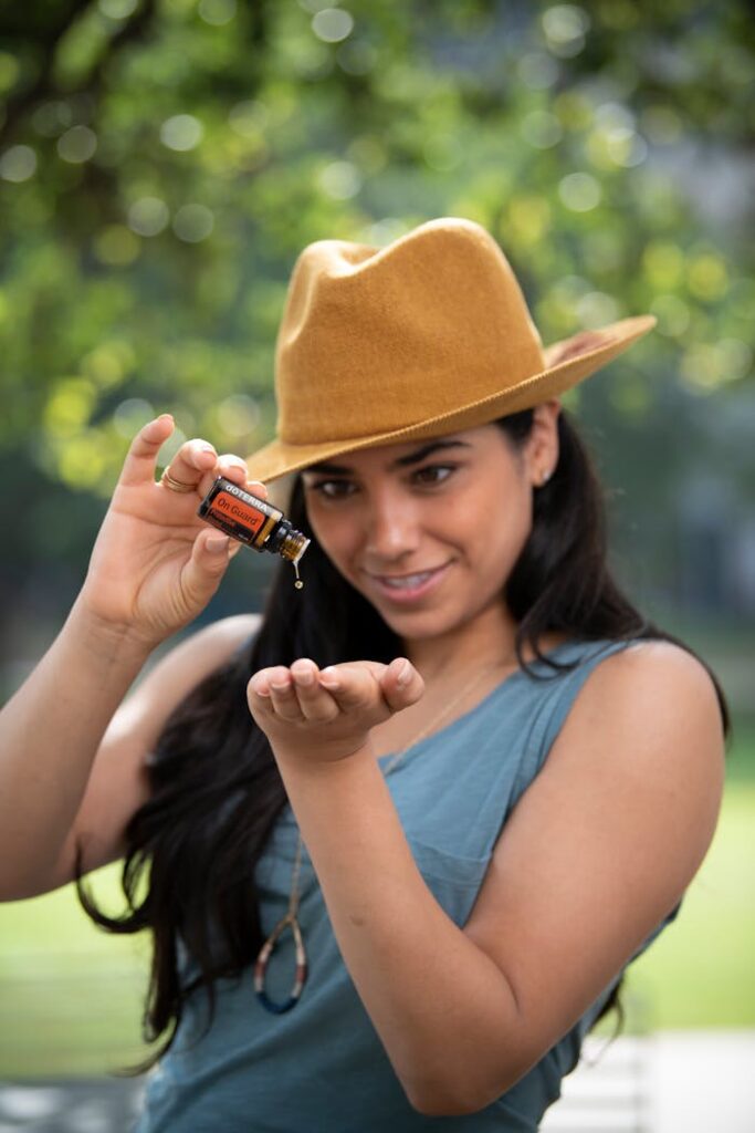 Smiling woman in a hat applying essential oil outdoors, promoting wellness.